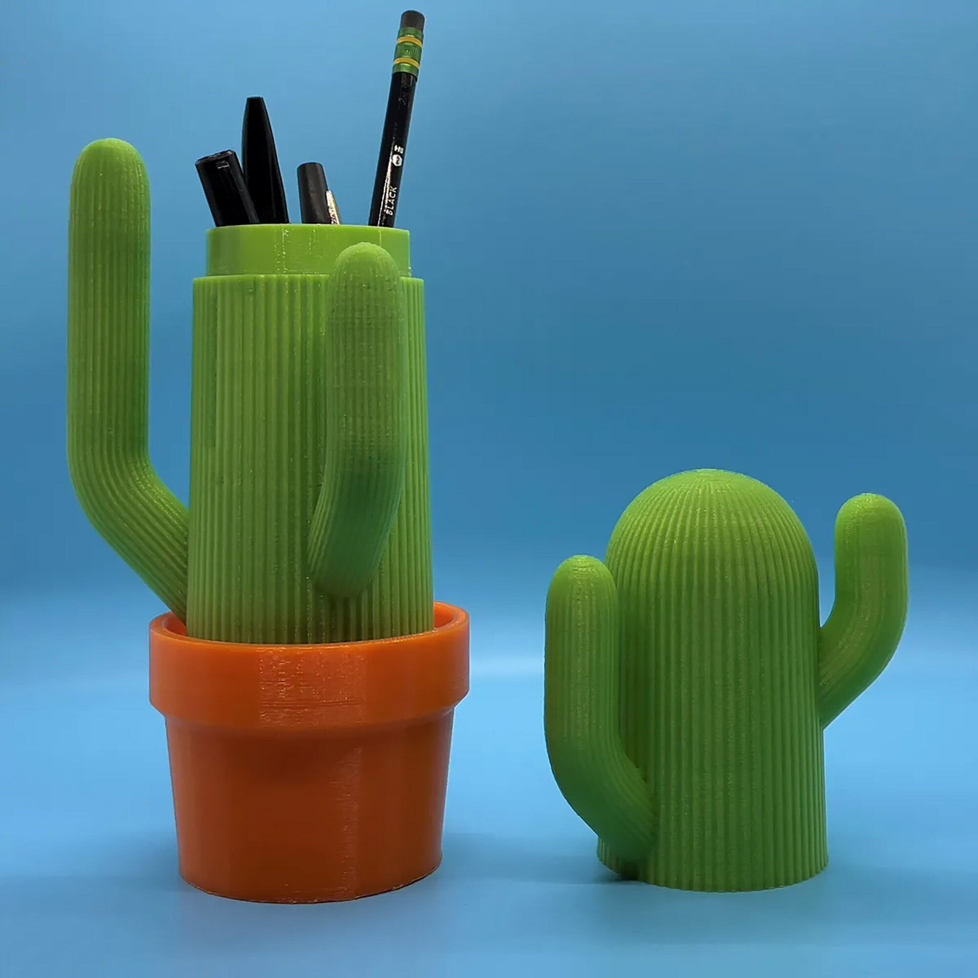 a cactus shaped pen holder next to a cactus plant