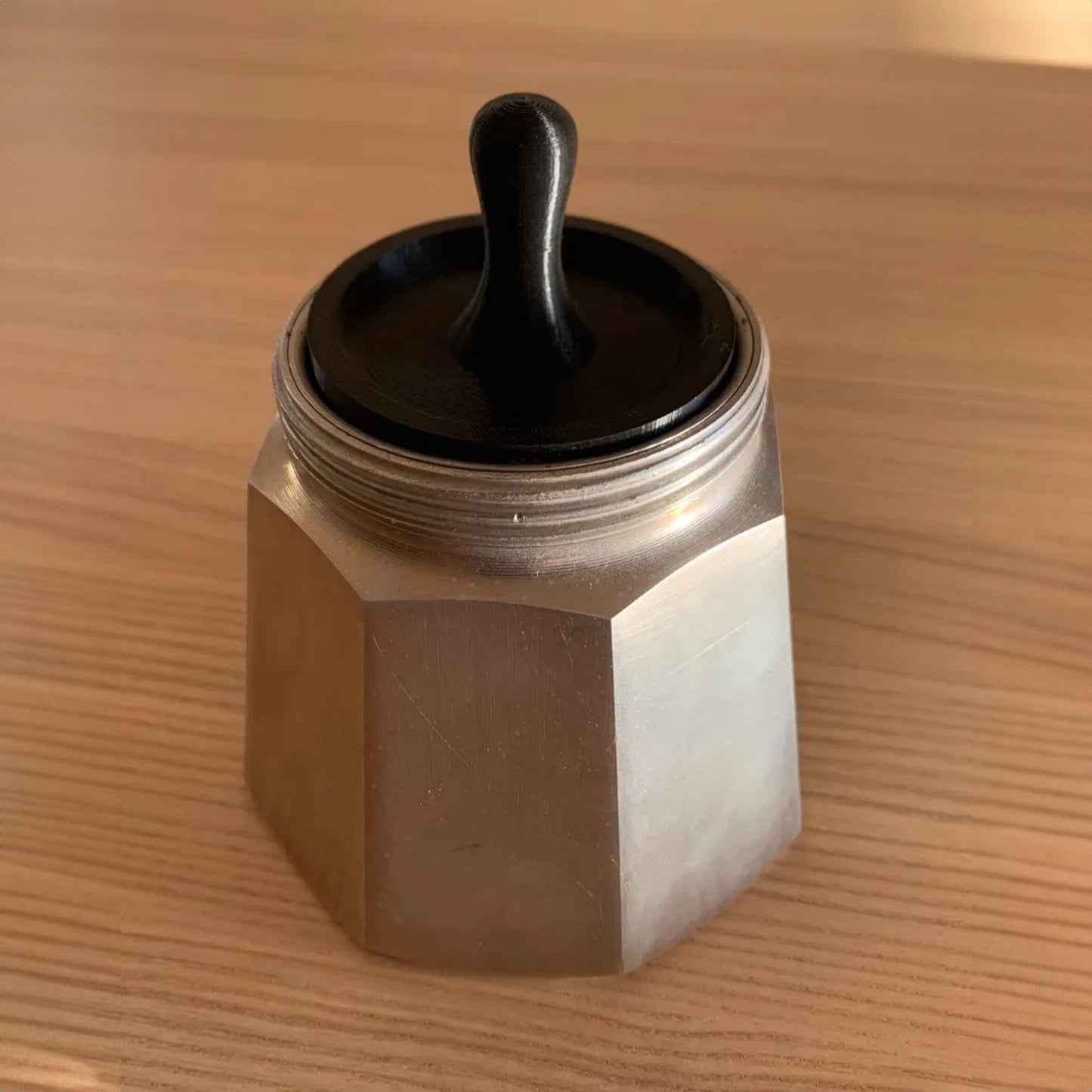 a metal container with a black lid on a wooden table