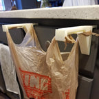 Pair of trash bag holders hooked over a kitchen cabinet door holding a grocery bag, view 2