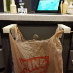 Pair of trash bag holders hooked over a kitchen cabinet door holding a grocery bag