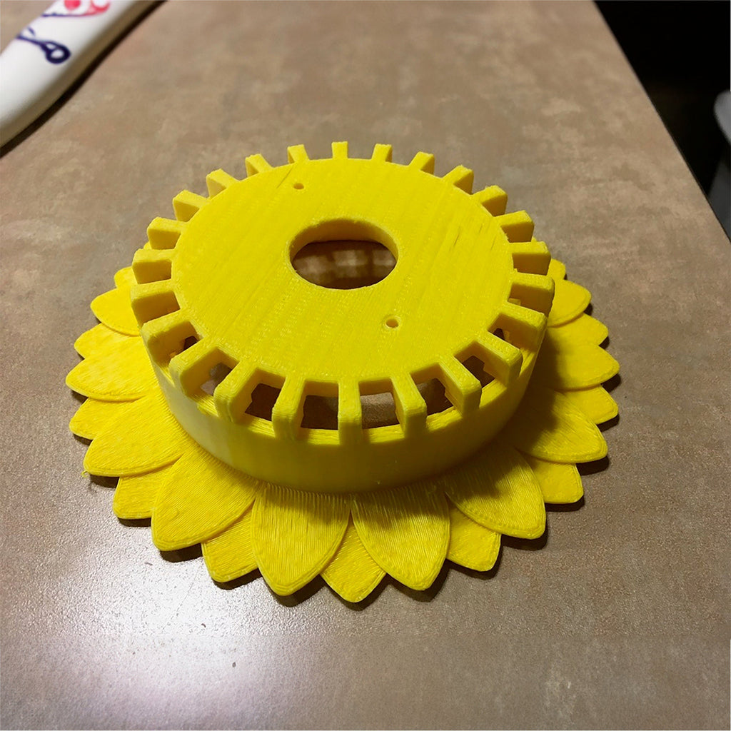 Sunflower stand with layered petals framing a puck-style Echo Dot speaker, view 3