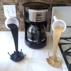 Floating coffee mug sculpture with a coffee stream pouring into a splash puddle