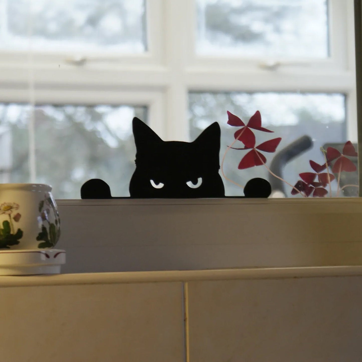 a black cat sitting on top of a counter next to a potted plant