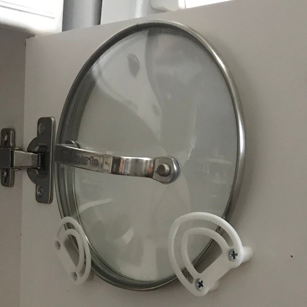 Pot lid holder clips mounted inside a kitchen cabinet door holding a glass lid, view 3