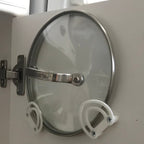 Pot lid holder clips mounted inside a kitchen cabinet door holding a glass lid, view 3