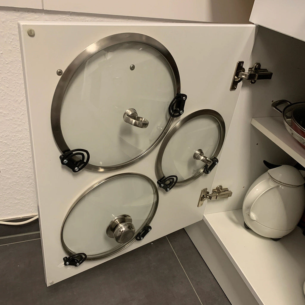 Pot lid holder clips mounted inside a kitchen cabinet door holding a glass lid, view 4