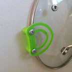 Pot lid holder clips mounted inside a kitchen cabinet door holding a glass lid, view 5