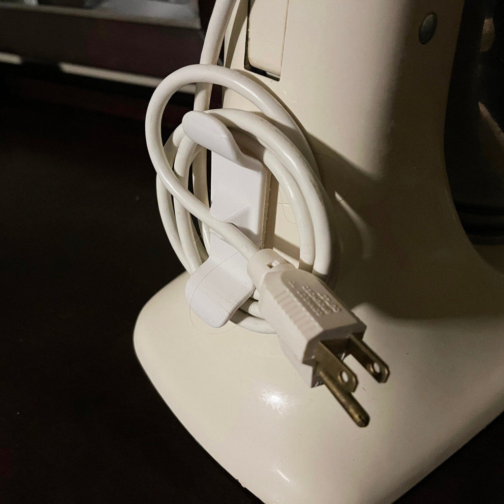 Adhesive twin-prong cord cleat on the back of a KitchenAid stand mixer