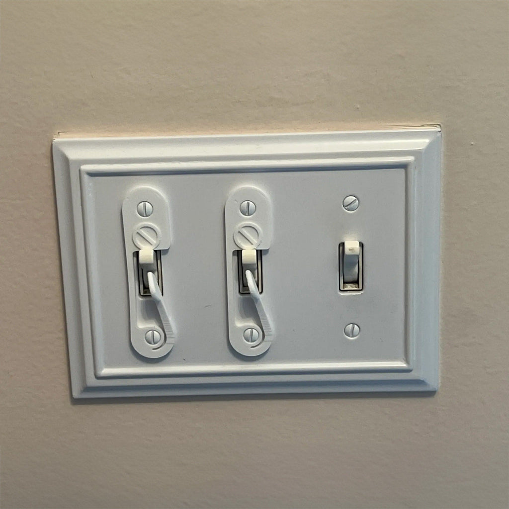 Light switch lock with pivoting arm and marked toggle cap on a wall switch, view 2