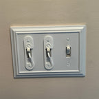 Light switch lock with pivoting arm and marked toggle cap on a wall switch, view 2