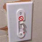 Light switch lock with pivoting arm and marked toggle cap on a wall switch, view 4
