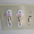 Light switch lock with pivoting arm and marked toggle cap on a wall switch