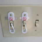 Light switch lock with pivoting arm and marked toggle cap on a wall switch