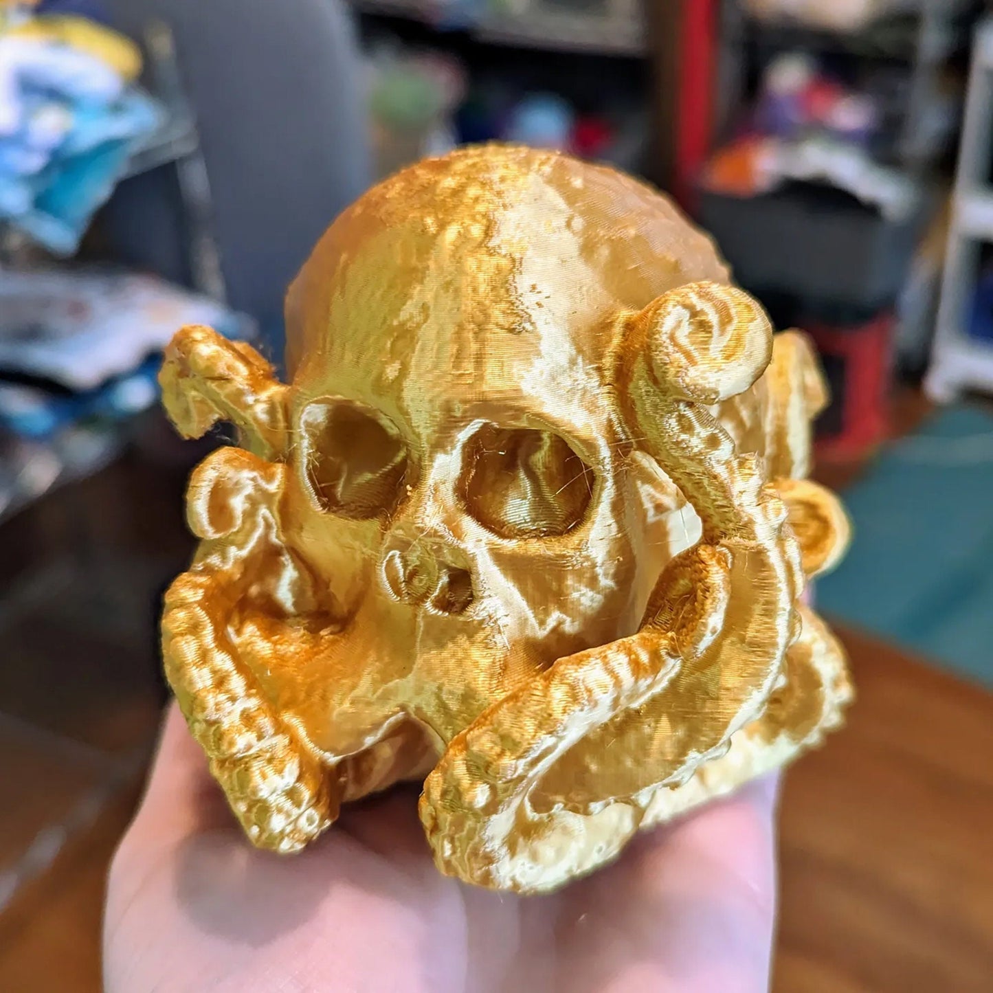 a hand holding a gold skull with an octopus on it