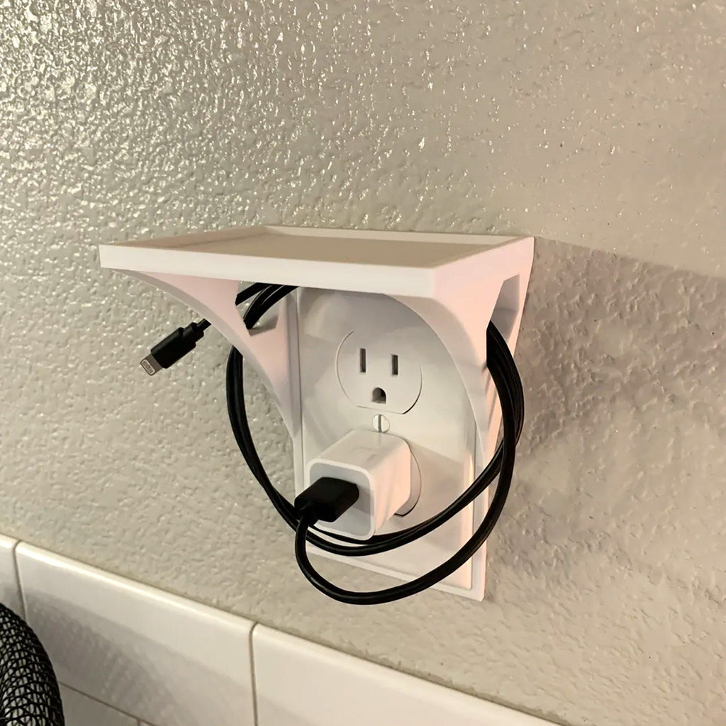 Outlet shelf mounted over a wall outlet holding a phone while it charges
