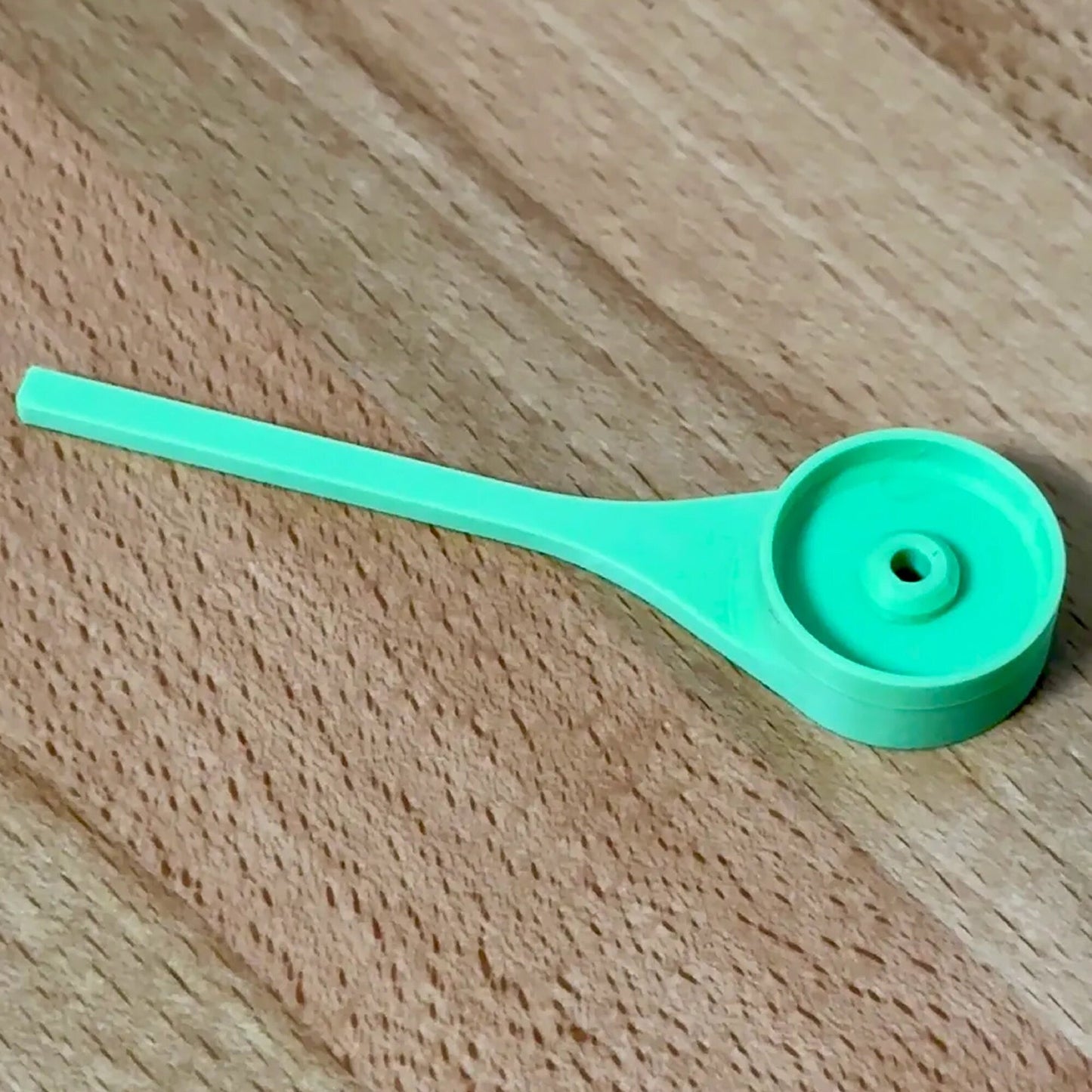 a green plastic spoon sitting on top of a wooden table