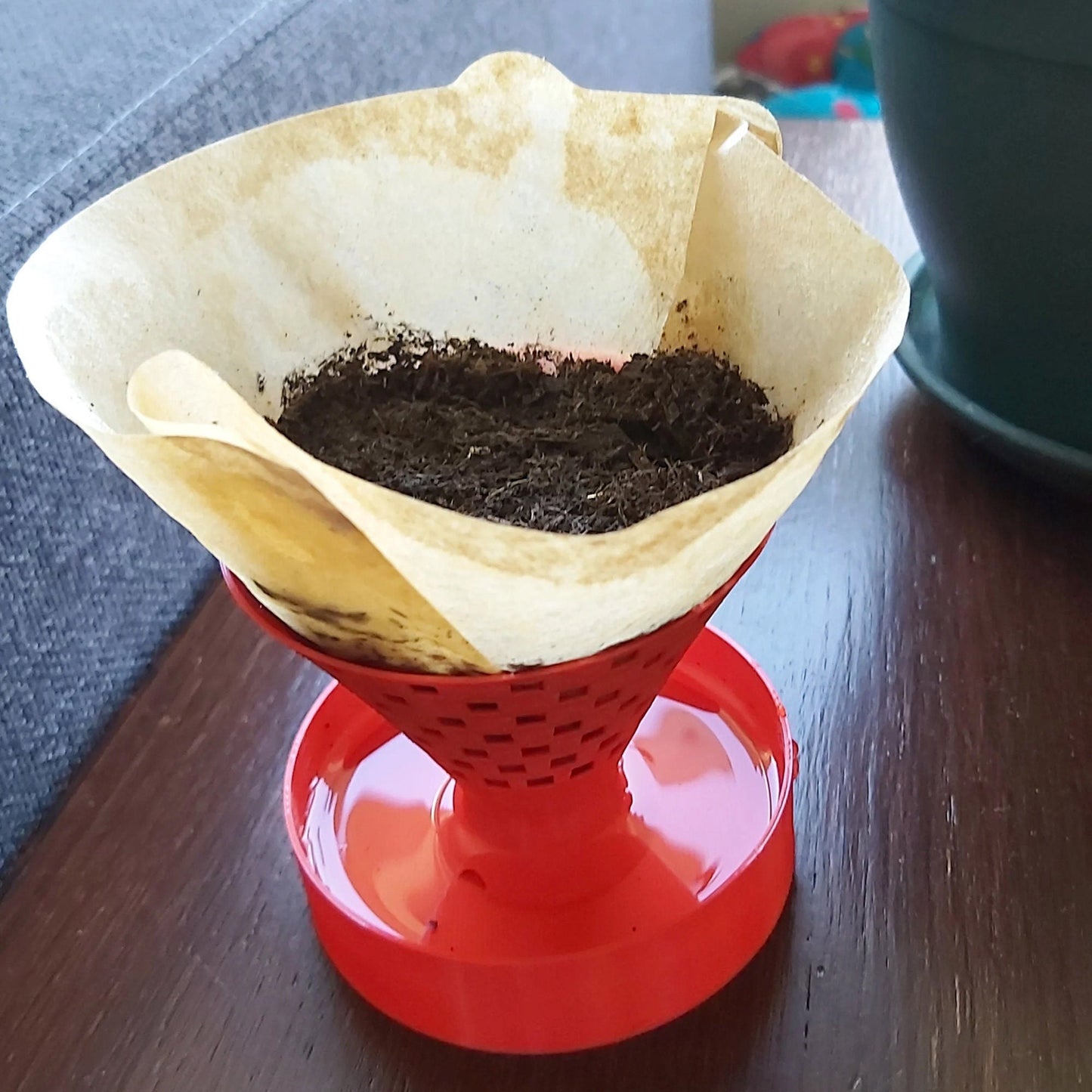 a red coffee pot filled with dirt on top of a wooden table