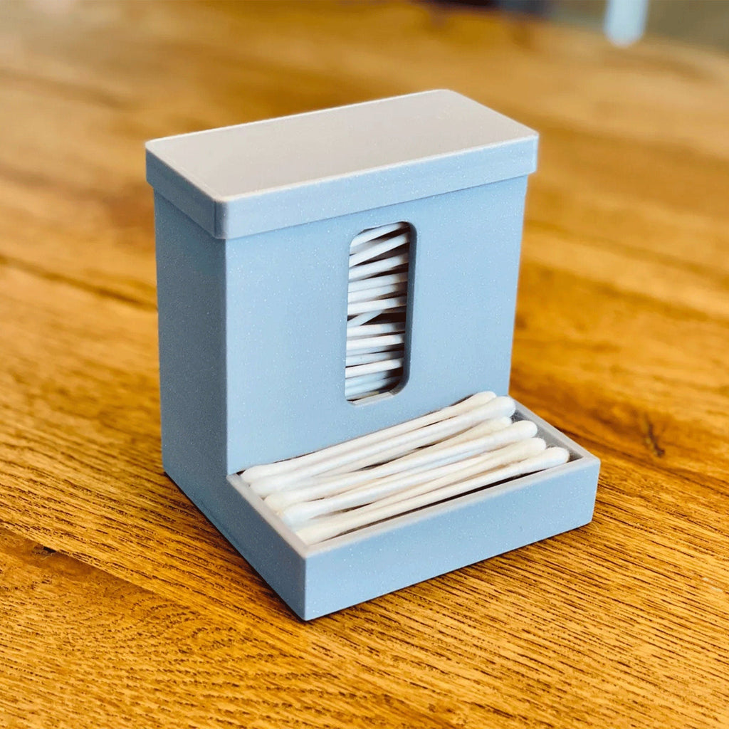 Covered cotton swab dispenser with a front catch tray on a bathroom vanity
