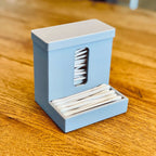 Covered cotton swab dispenser with a front catch tray on a bathroom vanity