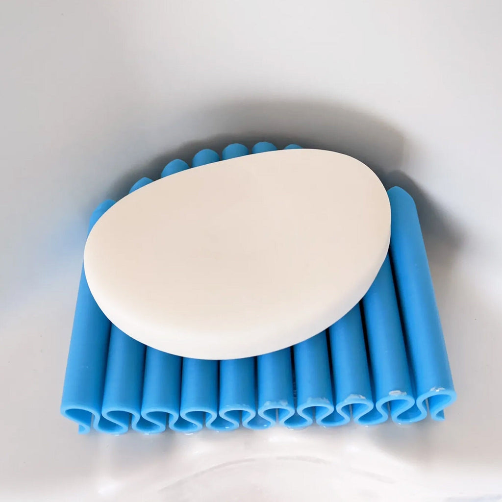 Self-draining ribbed soap dish holding a bar of soap by a sink, view 2