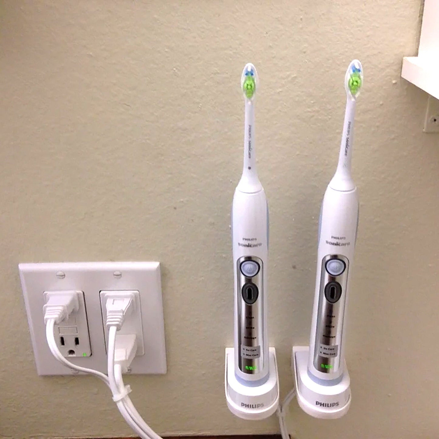 two electric toothbrushes plugged into a wall outlet