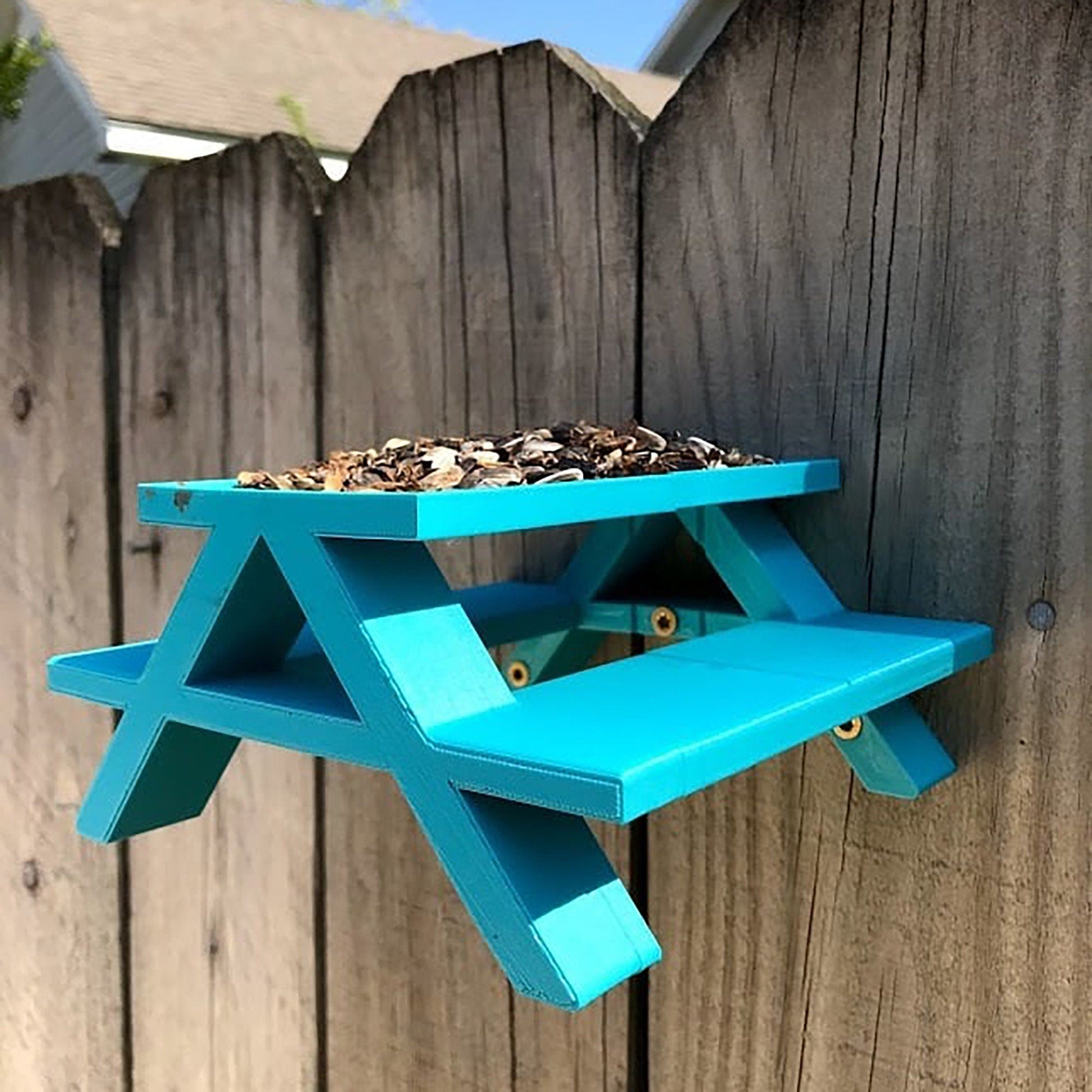 a blue bird feeder hanging on a wooden fence