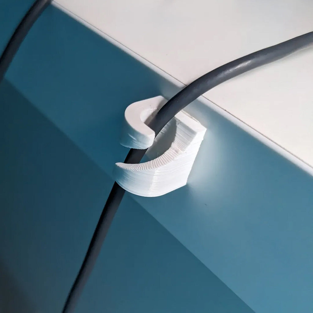 Adhesive cable clips holding USB and charging cords along a desk edge, view 2