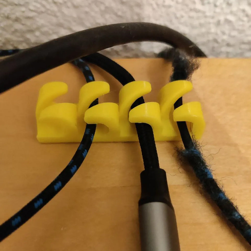 Adhesive cable clips holding USB and charging cords along a desk edge